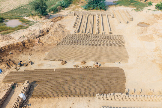 Aerial view of workers making traditional clay bricks at a factory with rows of drying bricks on sandy ground in Lahore, Punjab, Pakistan.
