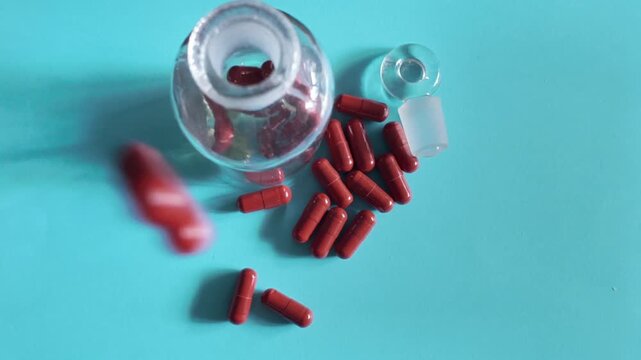 Red capsules beside an open glass medicine bottle in slow motion