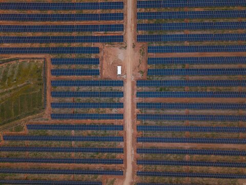 Aerial view of a large solar farm with rows of photovoltaic panels arranged in a grid pattern, separated by dirt access paths in Bonnievale, Western Cape, South Africa.