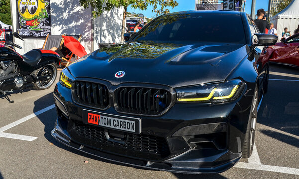 Aggressive black BMW M5 (F90) featuring carbon fiber body components and signature yellow DRL headlights, embodying modern high-performance super-sedan culture