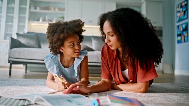 Girl drawing pencil mother lying living room floor. Multiracial home learning.