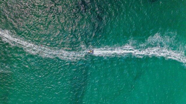 Aerial view of a jet ski speeding through the turquoise waters of Gordon's Bay, leaving a long white wake behind it in Cape Town, Western Cape, South Africa.