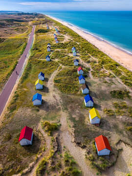 Aerial view of the iconic colorful beach huts scattered across the sand dunes along the coast in Gouville-sur-Mer, Normandy, France.