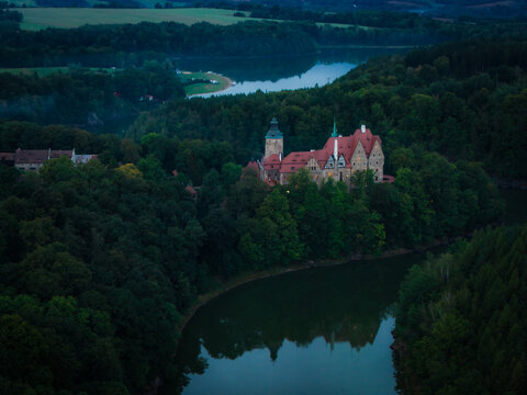 Aerial view of Czocha Castle surrounded by dense forest and a winding river at dusk in Sucha, Lower Silesia, Poland.