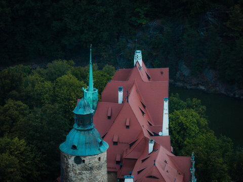 Aerial view of Czocha Castle with its distinctive red tiled roofs and green copper tower surrounded by dense forest and a river in Sucha, Wojewodztwo dolnoslaskie, Poland.