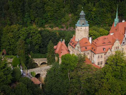 Aerial view of Czocha Castle with its distinctive stone tower and red-tiled roofs nestled within a lush forest in Sucha, Lower Silesia, Poland.