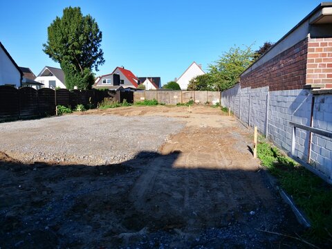 Prepared empty residential building plot with gravel base and fence boundaries in neighborhood