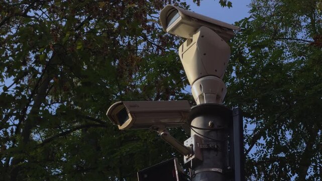 Close view of multiple CCTV cameras installed on a pole beside a sidewalk on private property, providing perimeter surveillance and security monitoring.