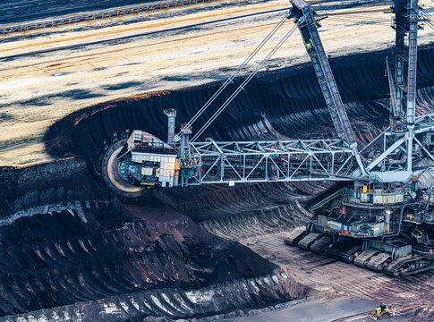 Aerial view of the massive bucket-wheel excavator operating within the deep brown earth of the Garzweiler surface mine in Juchen, North Rhine-Westphalia, Germany.