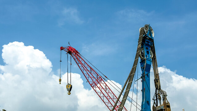 View of drilling equipment and a red crane against a blue sky with white clouds in India.