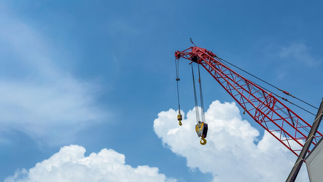 View of a red industrial crane with heavy hooks against a bright blue sky with white clouds in India.