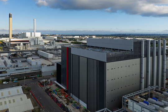 Aerial view of a modern data center building with metallic facade and industrial surroundings under a clear blue sky in the United Kingdom.