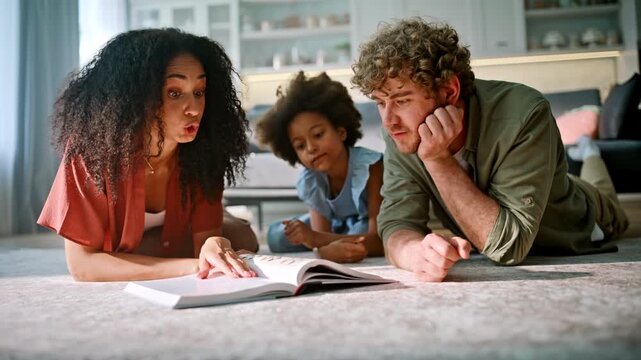 Mom explaining book daughter lying floor. Multiethnic family homework together.