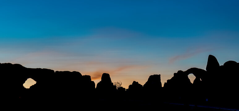 View of sandstone arches and rock formations silhouetted against a colorful sunrise sky in the Windows Section of Arches National Park near Moab, Utah.