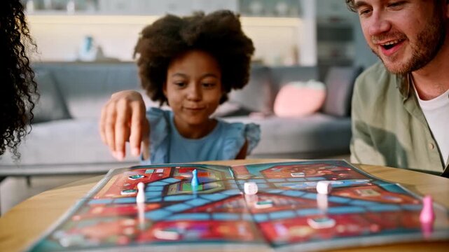 Dad rolling dice board game home. Multiracial family playing girl living room.