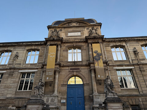 Stone facade of the Musee des Beaux-Arts de Rouen, featuring sculpted figures, a blue entrance door and exhibition banners - Rouen, France - September 5, 2026