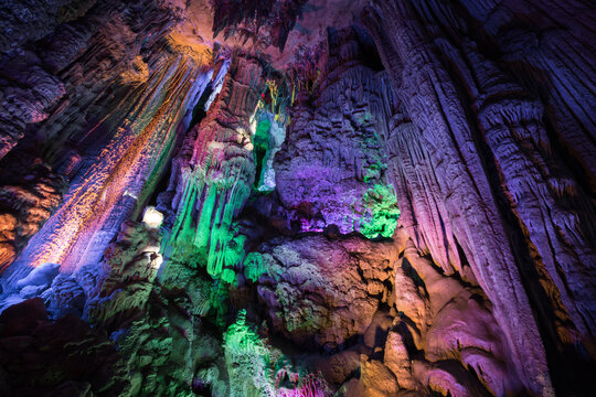 View of the colorful illuminated stalactites and stalagmites inside a limestone cave in Yangshuo, Guangxi, China.