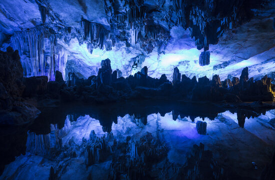 View of the illuminated stalactites and stalagmites reflecting in the calm water inside a cave in Yangshuo, Guangxi, China.