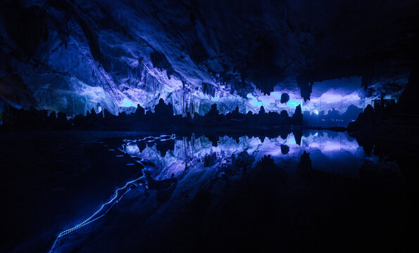 View of the illuminated stalactites and stalagmites reflecting in the calm water inside a cave in Yangshuo, Guangxi, China.