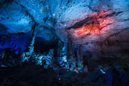 View of illuminated stalactites and stalagmites inside a limestone cave with vibrant blue and red lighting in Yangshuo, Guangxi, China.