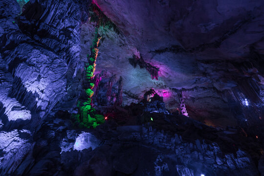 View of the illuminated stalactites and stalagmites inside a cave with vibrant purple and green lighting in Yangshuo, Guangxi, China.