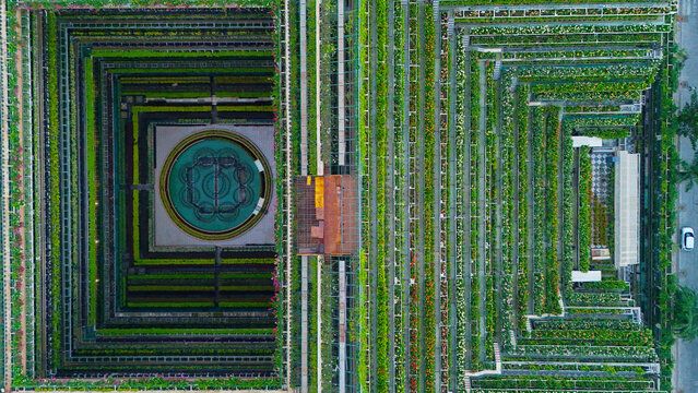 Aerial view of a symmetrical historic stepwell featuring intricate stone architecture, lush green terraced gardens, and a central circular water feature in Surat, Gujarat, India.