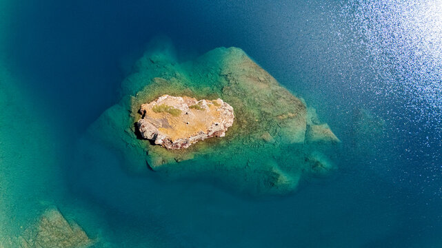 Aerial view of Maheen lake featuring a small, rocky island surrounded by crystal clear turquoise and deep blue water in Batakundi, Khyber Pakhtunkhwa, Pakistan.