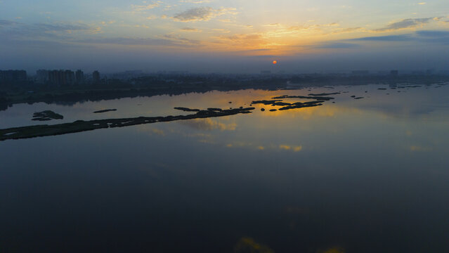 Aerial view of the Tapi River at sunset with reflections on the water, distant city skyline, and small sandbars in Surat, Gujarat, India.