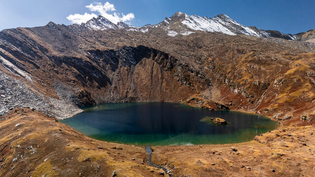 Aerial view of Maheen Lake surrounded by rugged rocky mountains with patches of snow and autumn-colored slopes in Batakundi, Khyber Pakhtunkhwa, Pakistan.