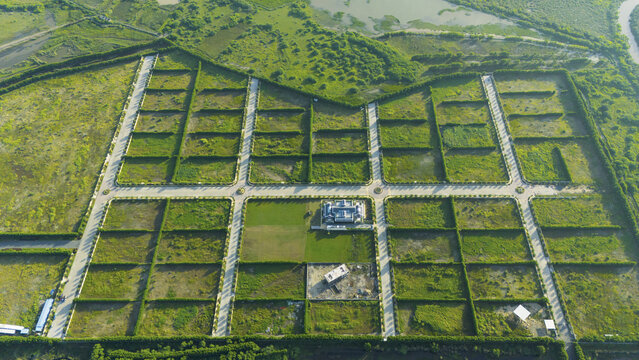 Aerial view of a planned land development with grid-like roads, green hedges, and construction plots in Surat, Gujarat, India.