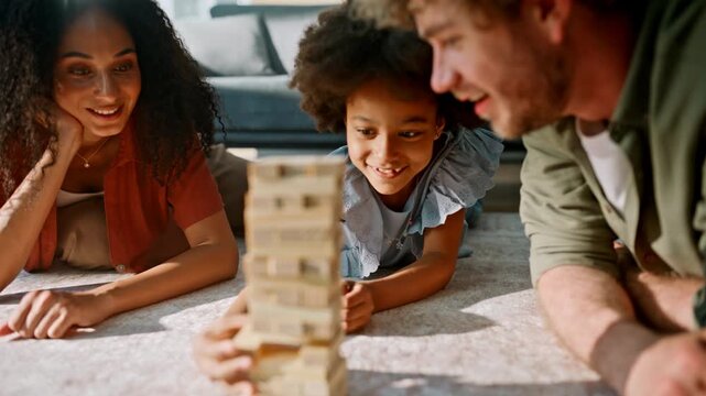 Wooden block tower collapsing family game. Multiethnic parents daughter smiling.