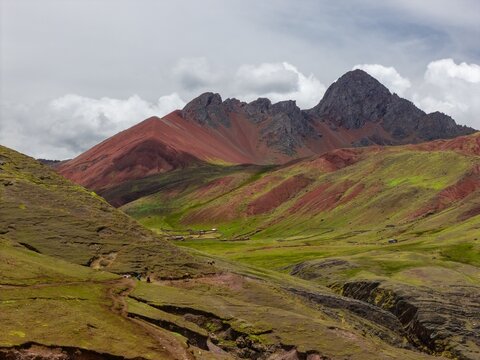 Aerial view of the vibrant Red Valley near Rainbow Mountain, featuring striking red-hued slopes, lush green valleys, and rugged Andean peaks in Cusco, Cuzco, Peru.