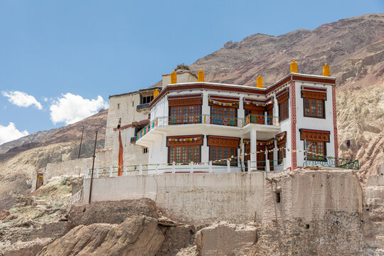 View of Charasa Gonpa, a traditional white monastery with wooden windows and colorful prayer flags, situated on a rocky outcrop against a mountain backdrop in Charasa, Ladakh, India.