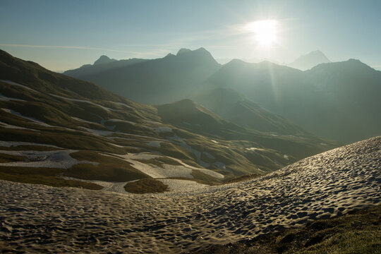 View of the Tour du Mont Blanc on the Italian Swiss border at Grand Col Ferret featuring rugged mountain slopes with patches of snow under bright sunlight, in the Swiss Val Ferret.