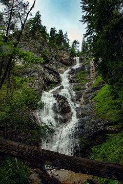 View of the Pollat waterfall cascading down rocky cliffs surrounded by lush pine forest and greenery in Schwangau, Bavaria, Germany.
