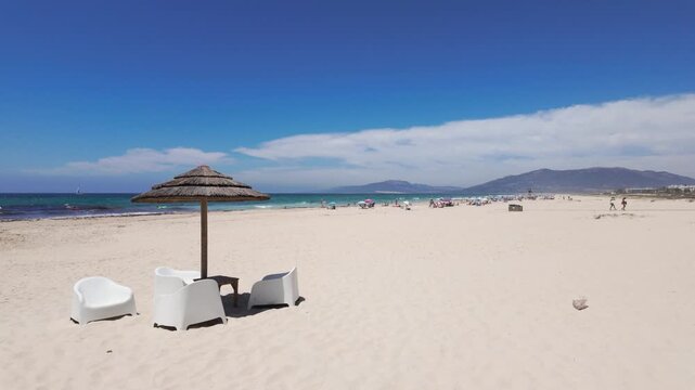 Straw parasol and white chairs alone on a wide empty beach