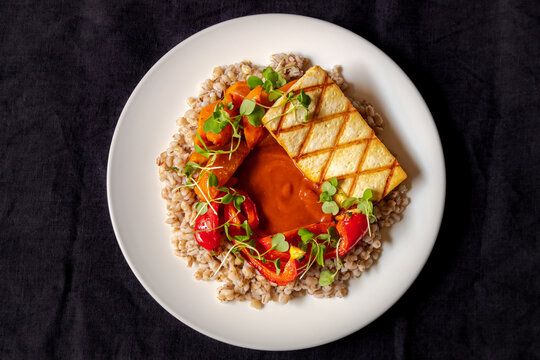 View of a plate featuring grilled tofu, roasted red peppers, roasted carrots, and grains garnished with fresh microgreens in Latvia.