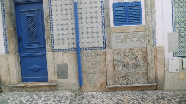 Historic blue door and patterned tile facade on quiet cobblestone street with soft daylight