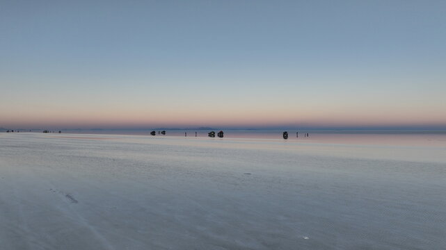 Aerial view of the vast Salar de Uyuni salt flats with a reflective surface and distant mountains under a soft twilight sky in Uyuni, Departamento de Potosi, Bolivia.