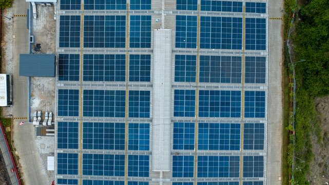 Aerial view of a warehouse roof covered with solar panels, showing the grid layout of the photovoltaic modules and surrounding industrial infrastructure in Bhiwandi, Maharashtra, India.