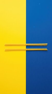 Top view photo of two uncooked yellow spaghetti strands arranged horizontally on a split background, half bright yellow and half deep blue, color block, nobody, spaghetti