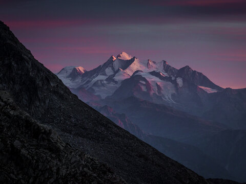 Aerial view of Aletsch Glacier with snow-capped peaks illuminated by vibrant alpenglow under a purple sunset sky in Fieschertal, Valais, Switzerland.