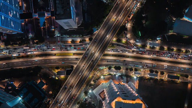Aerial view of a busy highway interchange illuminated at night with heavy traffic flow and urban buildings in Jakarta, Indonesia.