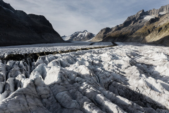 Aerial view of Aletsch Glacier with deep crevasses and rugged ice formations surrounded by towering snow-capped mountains in Fieschertal, Valais, Switzerland.