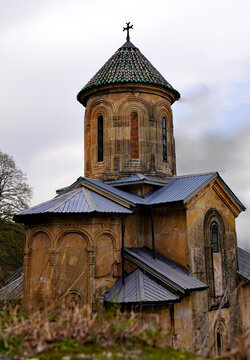 A low-angle view showcases a medieval stone Georgian Orthodox church featuring an ornate drum and conical dome surmounted by an iron cross under an overcast sky in Georgia