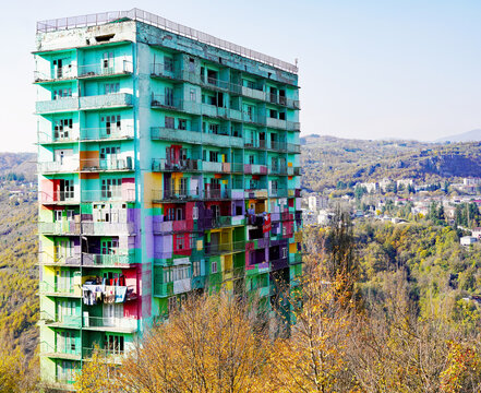 A multi-story Soviet-era residential apartment tower, painted in a patchwork of bright multicolored balconies, rises above autumnal hillsides in the mining town of Chiatura, Georgia