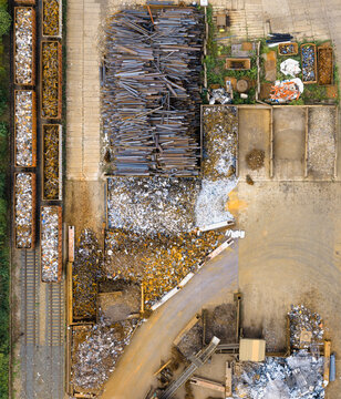 Aerial view of a scrap metal recycling facility with piles of industrial waste, metal bars, and train cars loaded with scrap in Saalfeld, Thuringia, Germany.