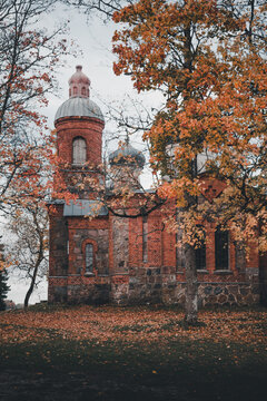 View of the historic red brick and stone Plaani Church surrounded by vibrant autumn foliage and fallen leaves in Plaani, Voru County, Estonia.