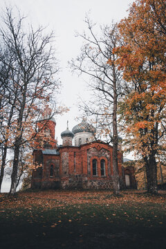 View of the historic Plaani Church of the Mother of God with its red brick walls and onion domes surrounded by vibrant autumn foliage in Plaani, Voru County, Estonia.