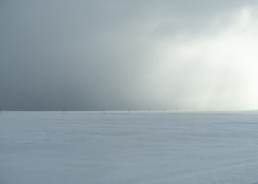 View of a vast, snow-covered landscape under a dramatic, overcast sky with a line of utility poles stretching into the distance in Myrdalshreppur, Iceland.